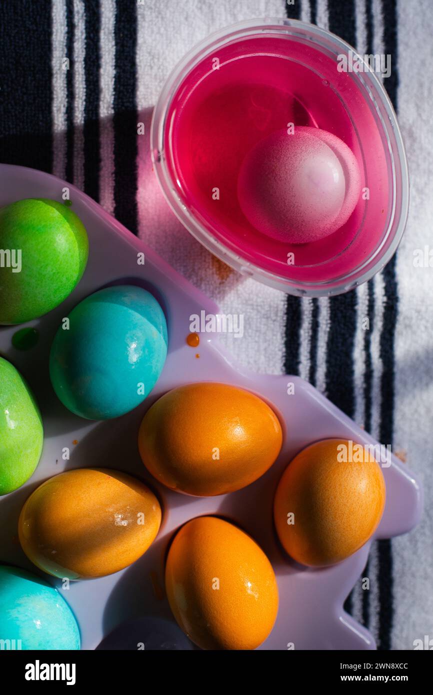 Gros plan de l'œuf dans une tasse de colorant alimentaire rose sur un torchon à vaisselle rayé Banque D'Images