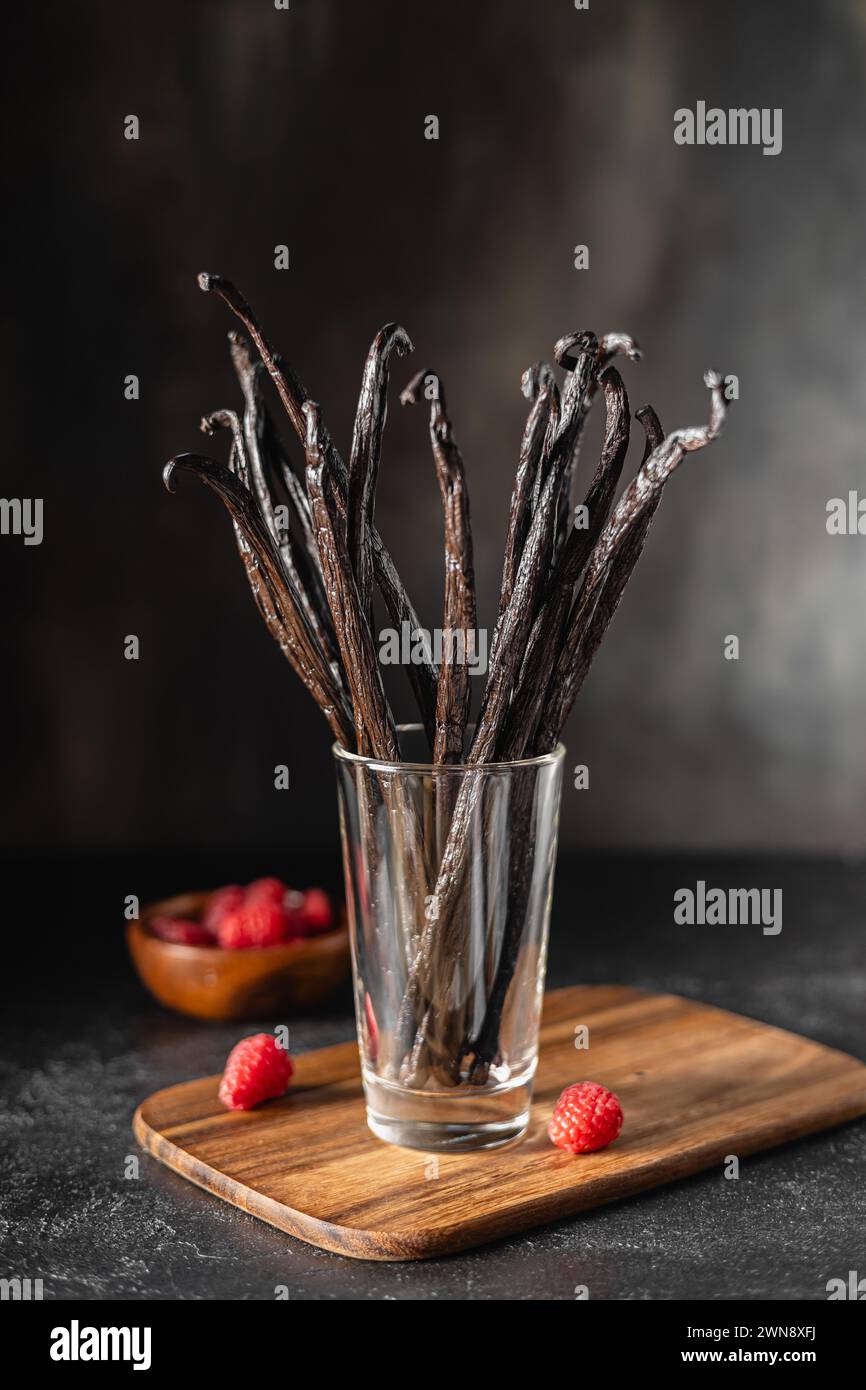 Haricots de vanille dans le verre sur une planche de bois et framboises Banque D'Images