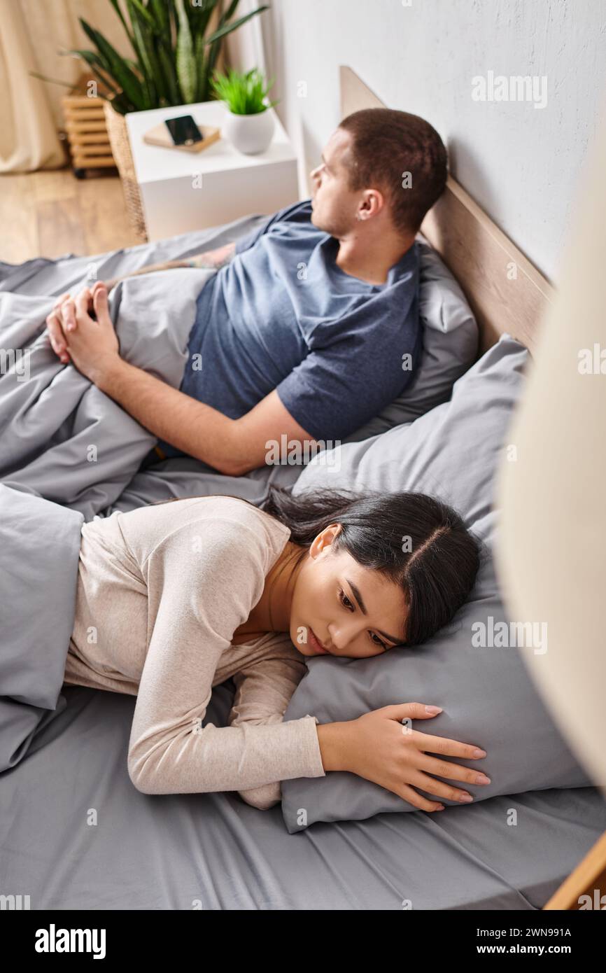 vue en angle élevé d'un couple interracial jeune et bouleversé couché sur le lit à la maison, troubles familiaux Banque D'Images
