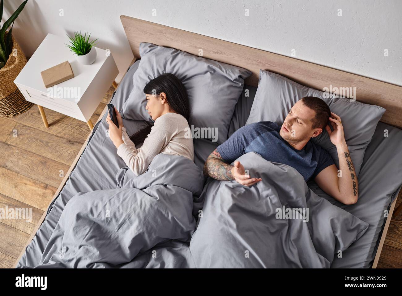 jeune femme asiatique regardant dans le smartphone du mari couché sur le lit à la maison, concept de conflit familial Banque D'Images