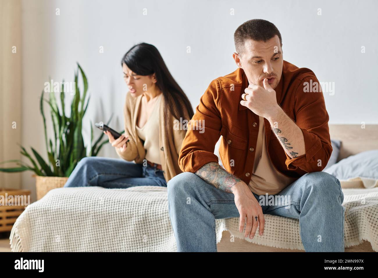 femme asiatique choquée regardant smartphone près de mari bouleversé dans la chambre ta maison, malentendu Banque D'Images