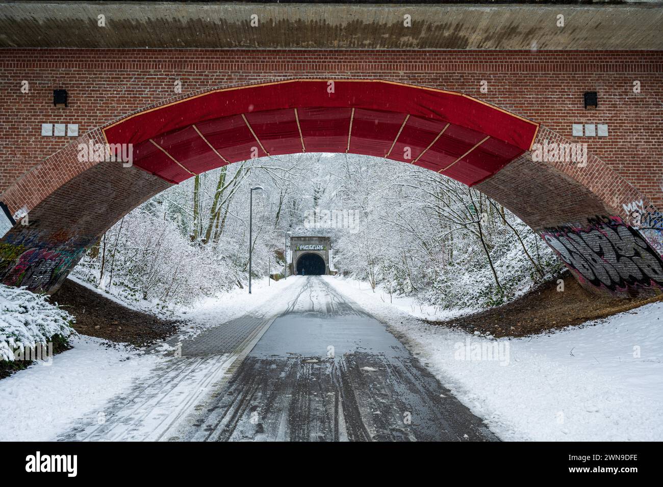 Un pont rouge enjambe une route enneigée, entourée d'arbres enneigés et de graffitis, Nordbahntrasse, Elberfeld, Wuppertal, Bergisches Land, Nord Banque D'Images