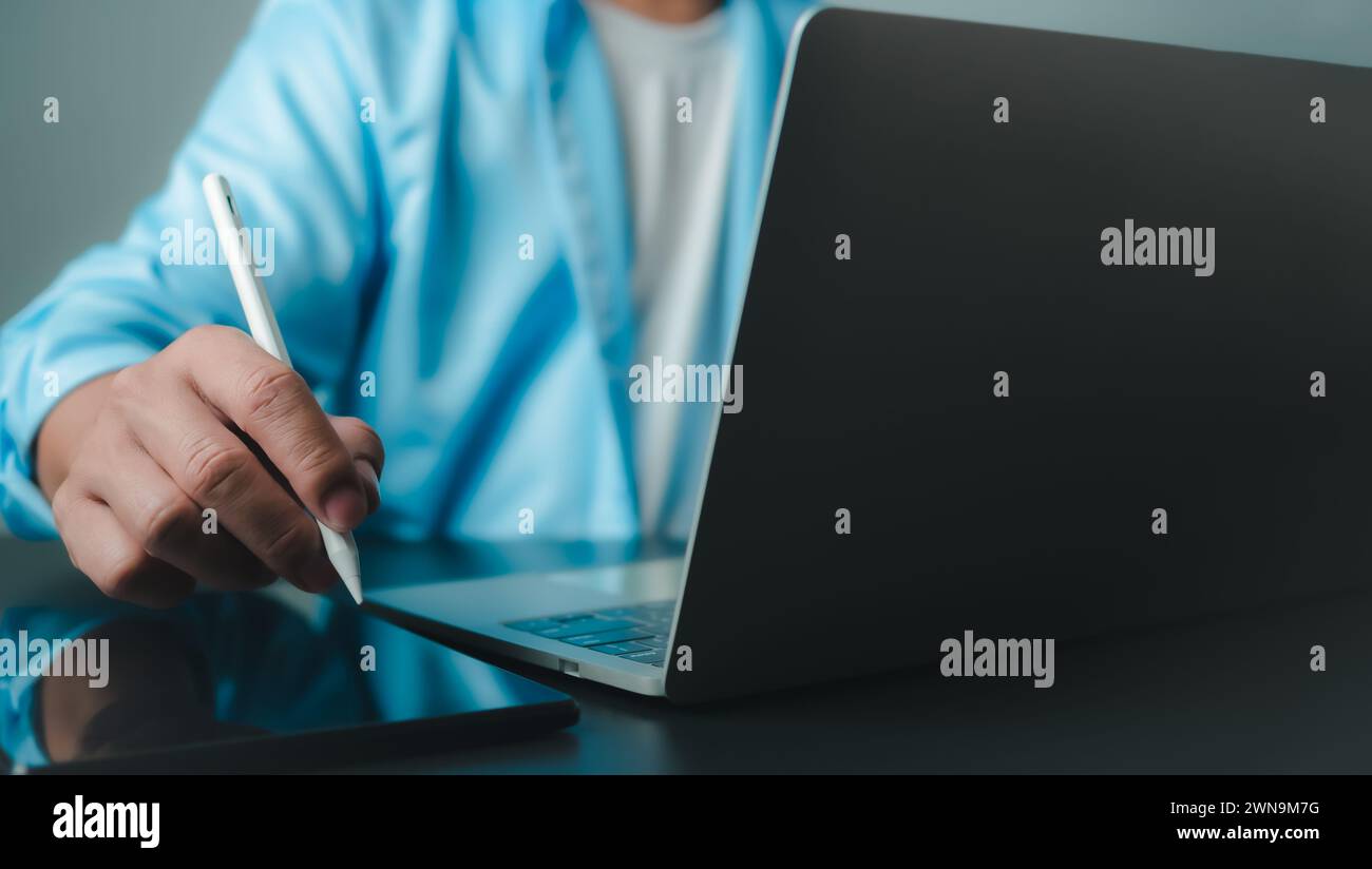 Homme d'affaires en costume noir travaillant sur ordinateur portable et tablette, toucher de main sur tablette au bureau avec fond sombre, travail en ligne, gros plan, copie s. Banque D'Images