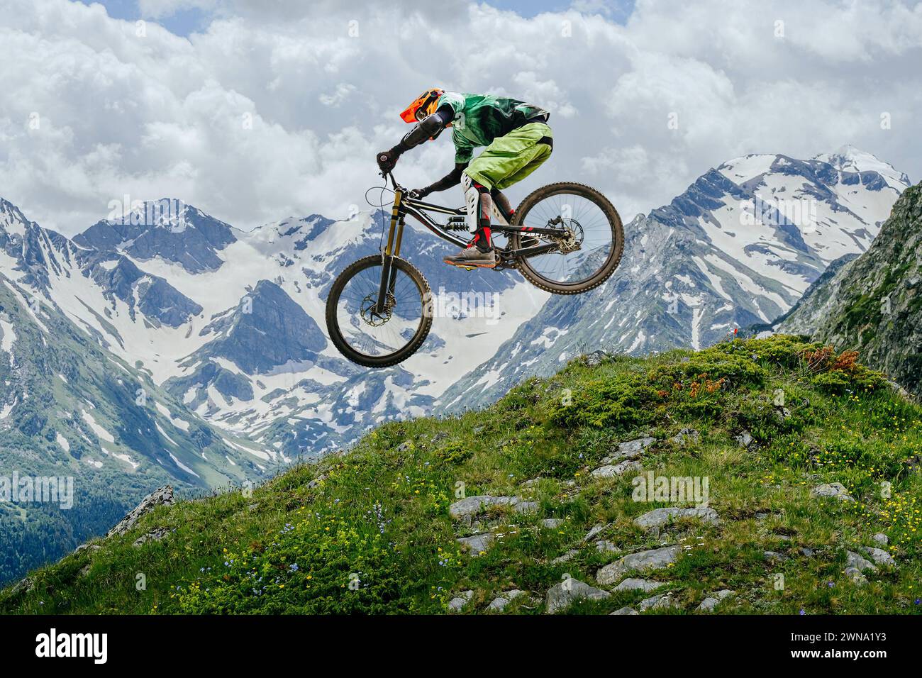 Le VTT a sauté, volant en plein air sur fond de sommets enneigés et de verdure luxuriante. compétition de descente Banque D'Images