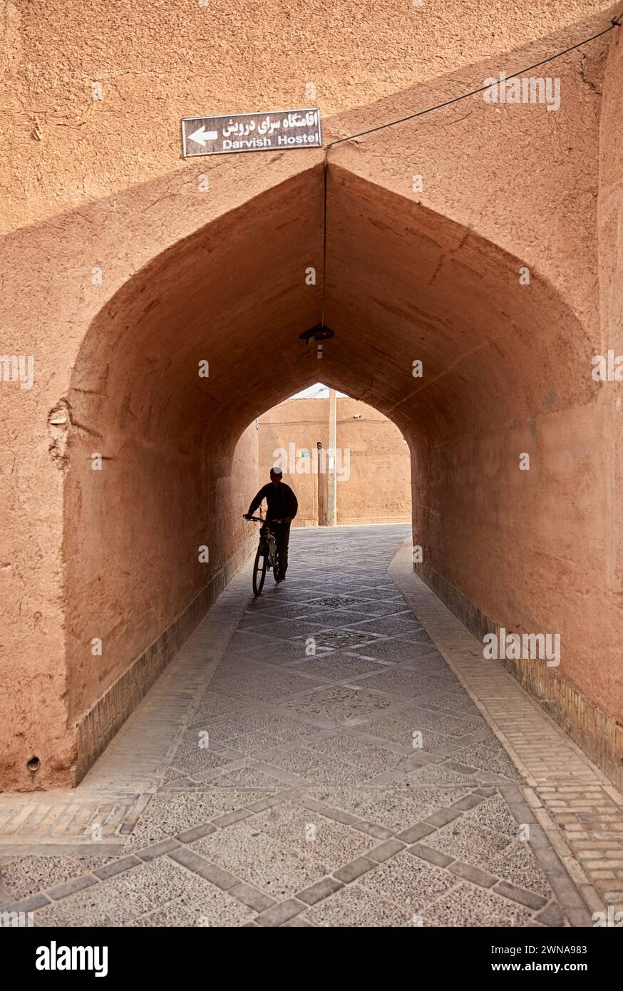 Un garçon fait du vélo dans une rue étroite à travers une arche dans le quartier historique de Fahadan à Yazd, en Iran. Banque D'Images