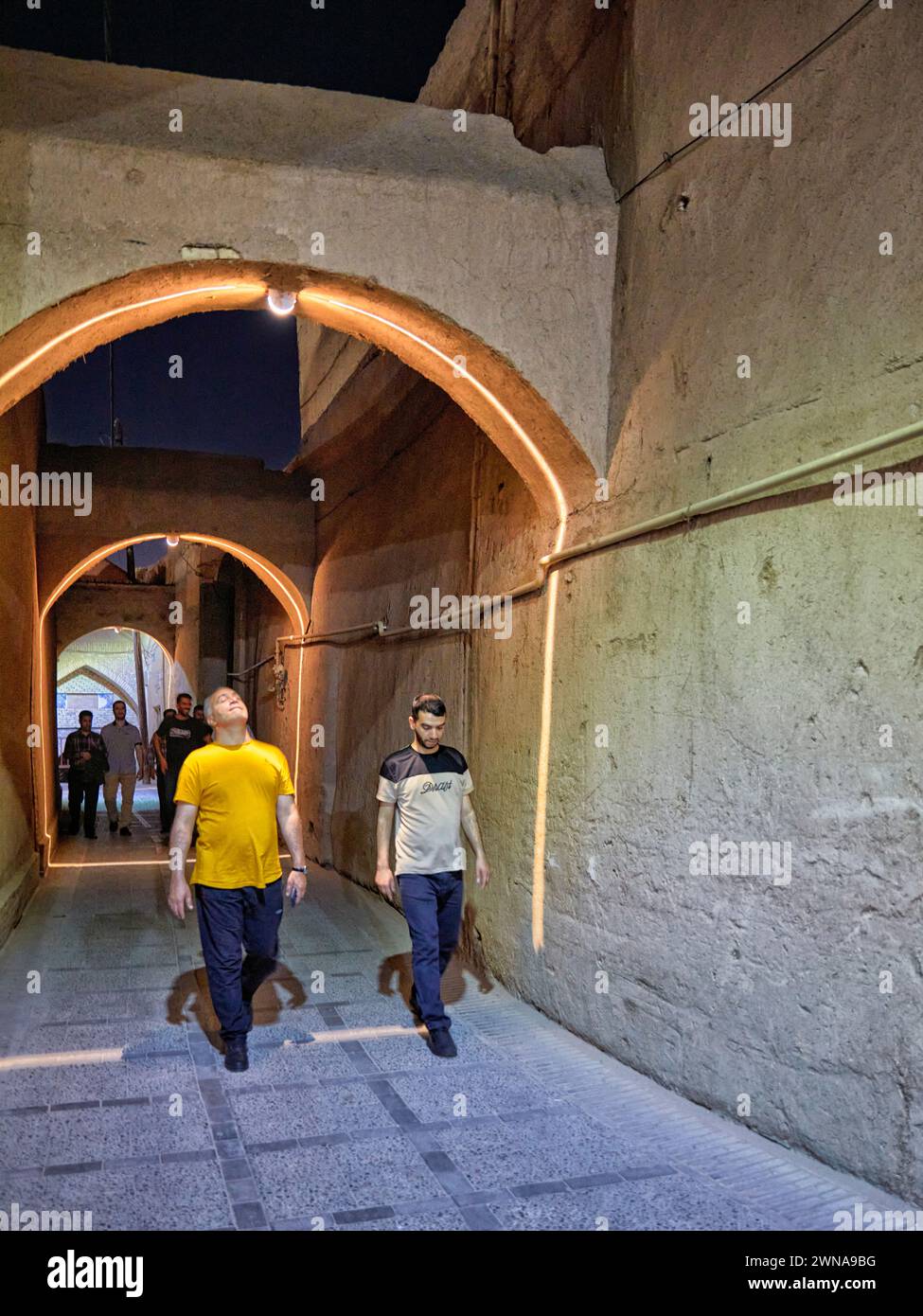 Les gens marchent dans une rue étroite avec des arcs brillamment illuminés la nuit dans le quartier historique de Fahadan à Yazd, en Iran. Banque D'Images