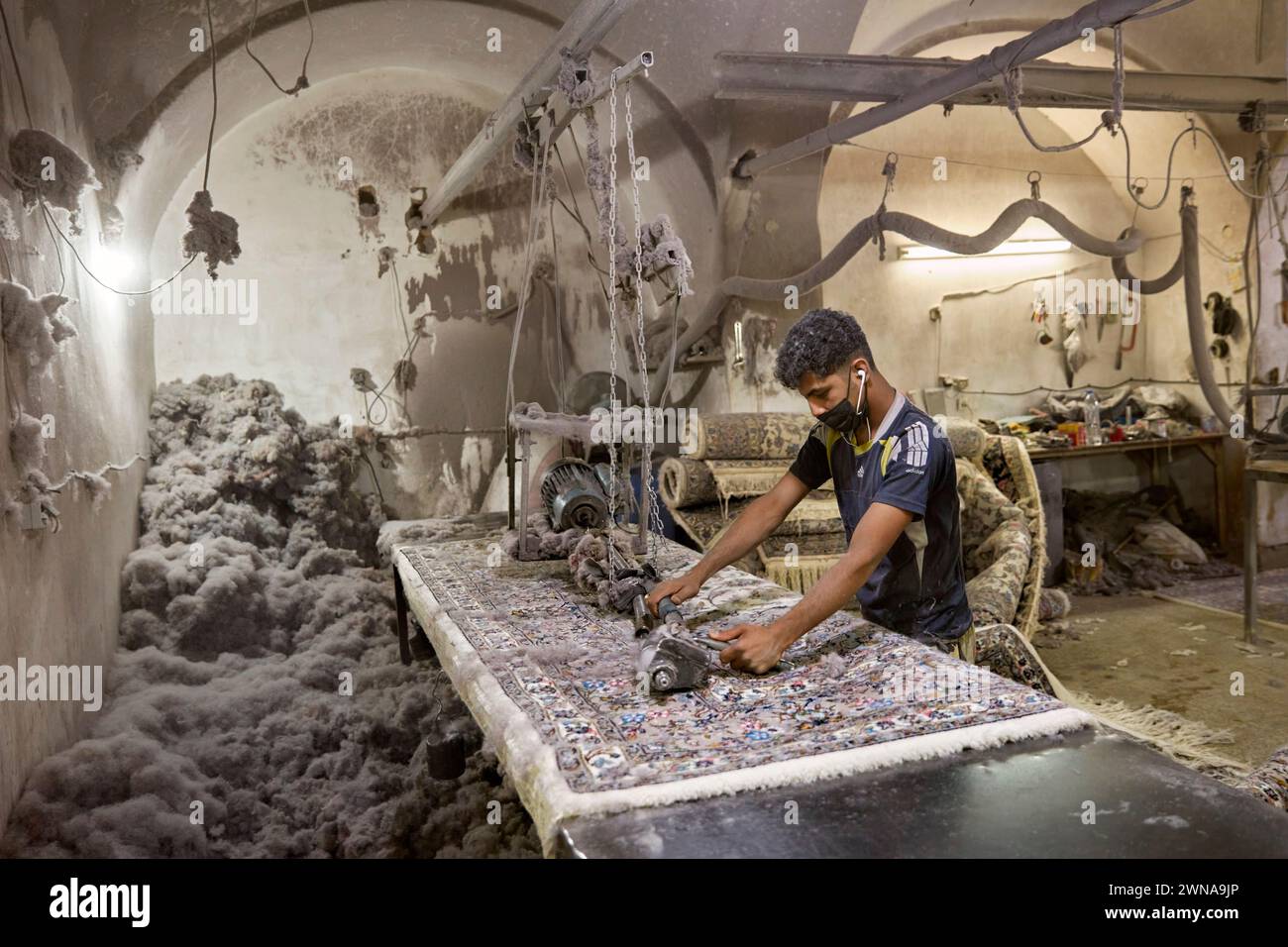 Un jeune homme travaille dans un petit atelier de fabrication de tapis. Yazd, Iran. Banque D'Images