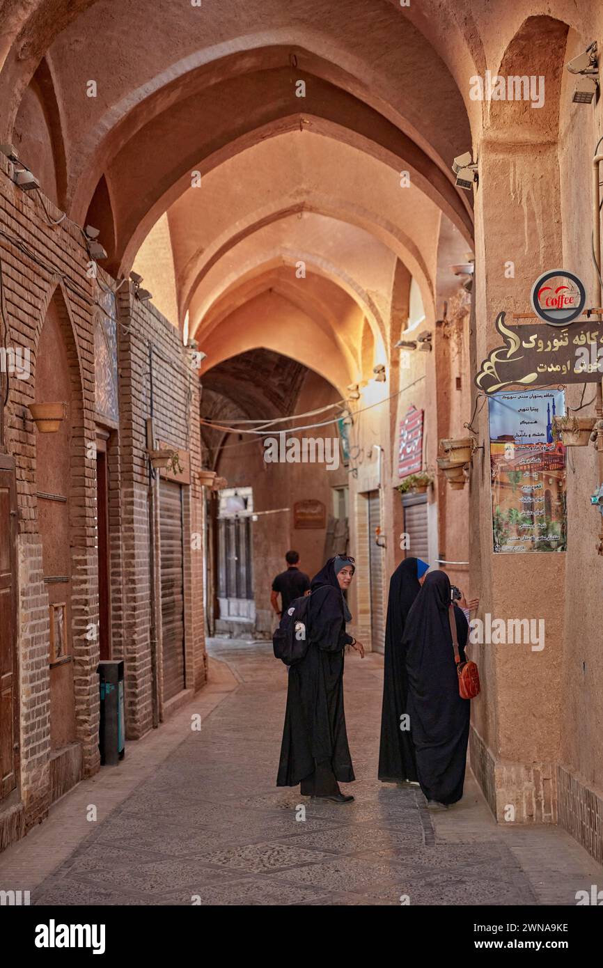 Trois femmes de Chadors marchent dans une rue étroite couverte de la vieille ville de Yazd, en Iran. Banque D'Images