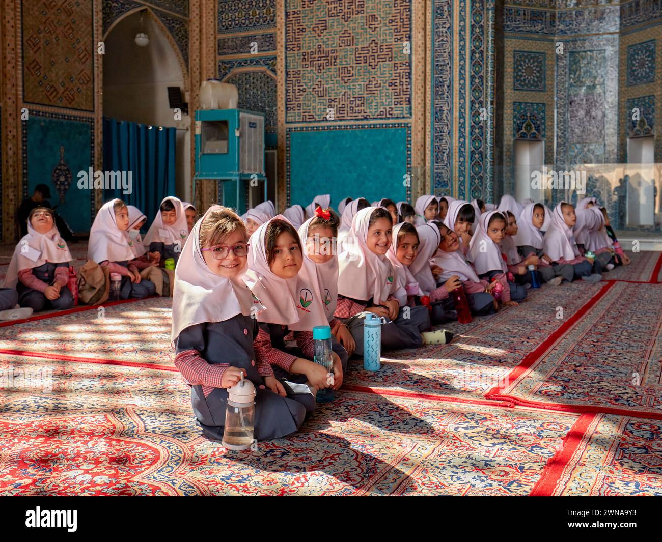 De petites écolières iraniennes en uniforme scolaire avec des hijabs roses sont assises sur le sol recouvert de moquette dans la mosquée Jameh de Yazd, mosquée chiite du XIVe siècle. Yazd, Iran. Banque D'Images
