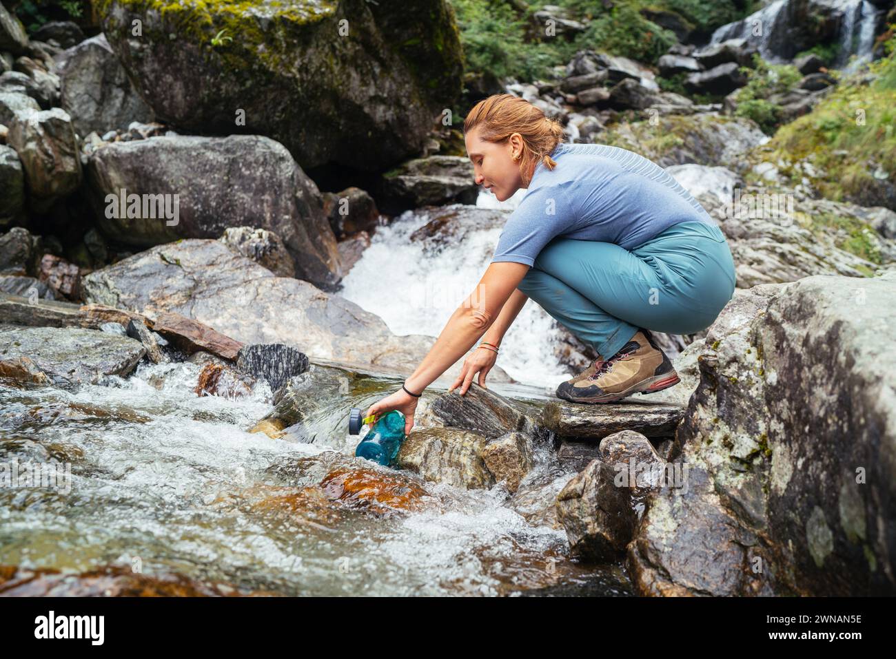 Jeune femme trekker traversant la rivière de montagne et remplissant l'eau douce ip dans la bouteille touristique pendant le trek du parc national Makalu Barun au Népal. Montagne h Banque D'Images