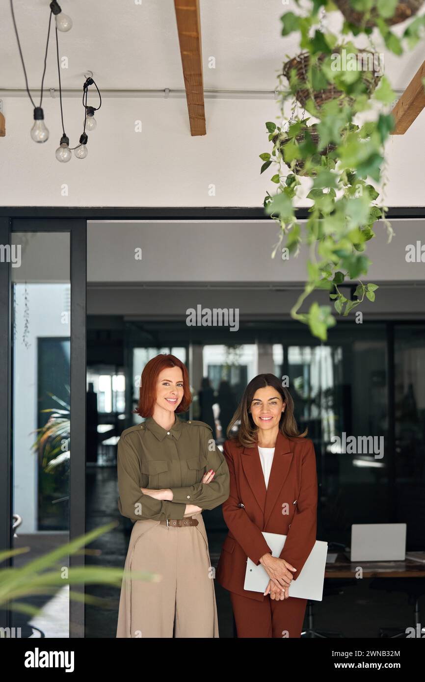 Deux joyeuses femmes d'affaires souriantes debout au travail dans le bureau. Portrait vertical. Banque D'Images