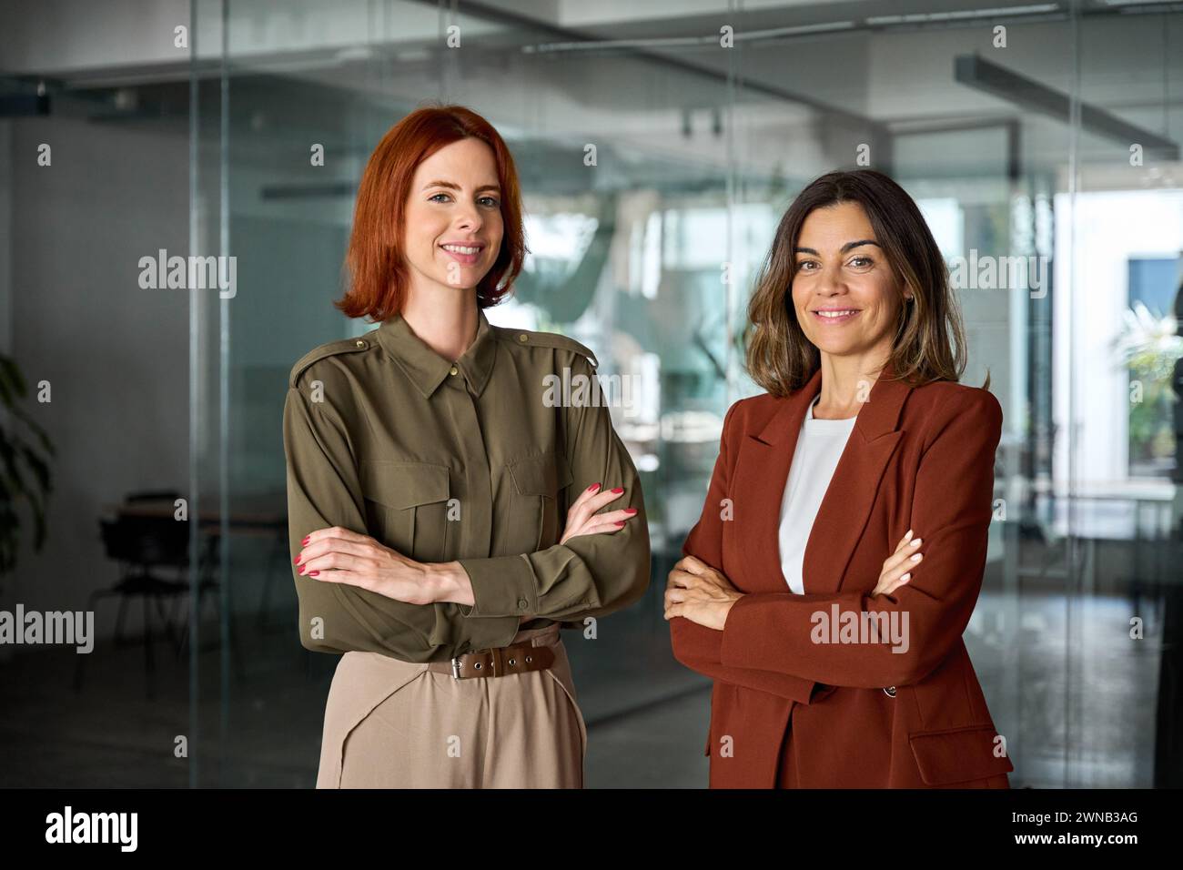Deux femmes d'affaires souriantes et confiantes debout les bras croisés dans le bureau, portrait. Banque D'Images