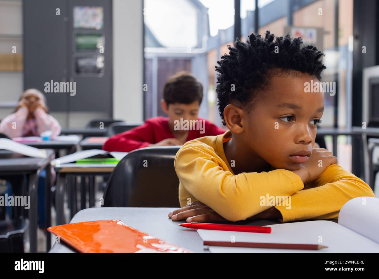 Garçon afro-américain dans une chemise jaune semble triste dans un cadre de classe avec espace de copie Banque D'Images