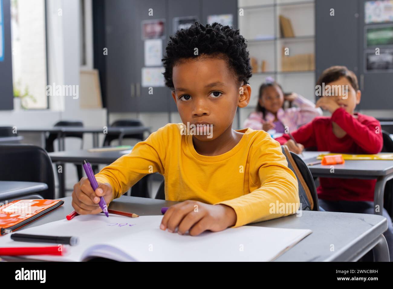 Garçon afro-américain dans une chemise jaune dessine dans une salle de classe d'école Banque D'Images