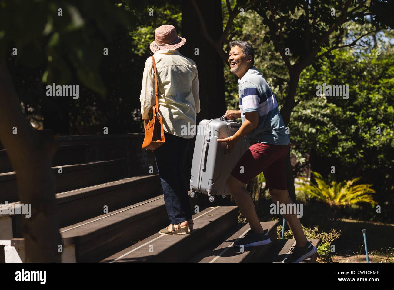 Femme biraciale senior et homme biracial monter les marches extérieures, homme tirant une valise Banque D'Images