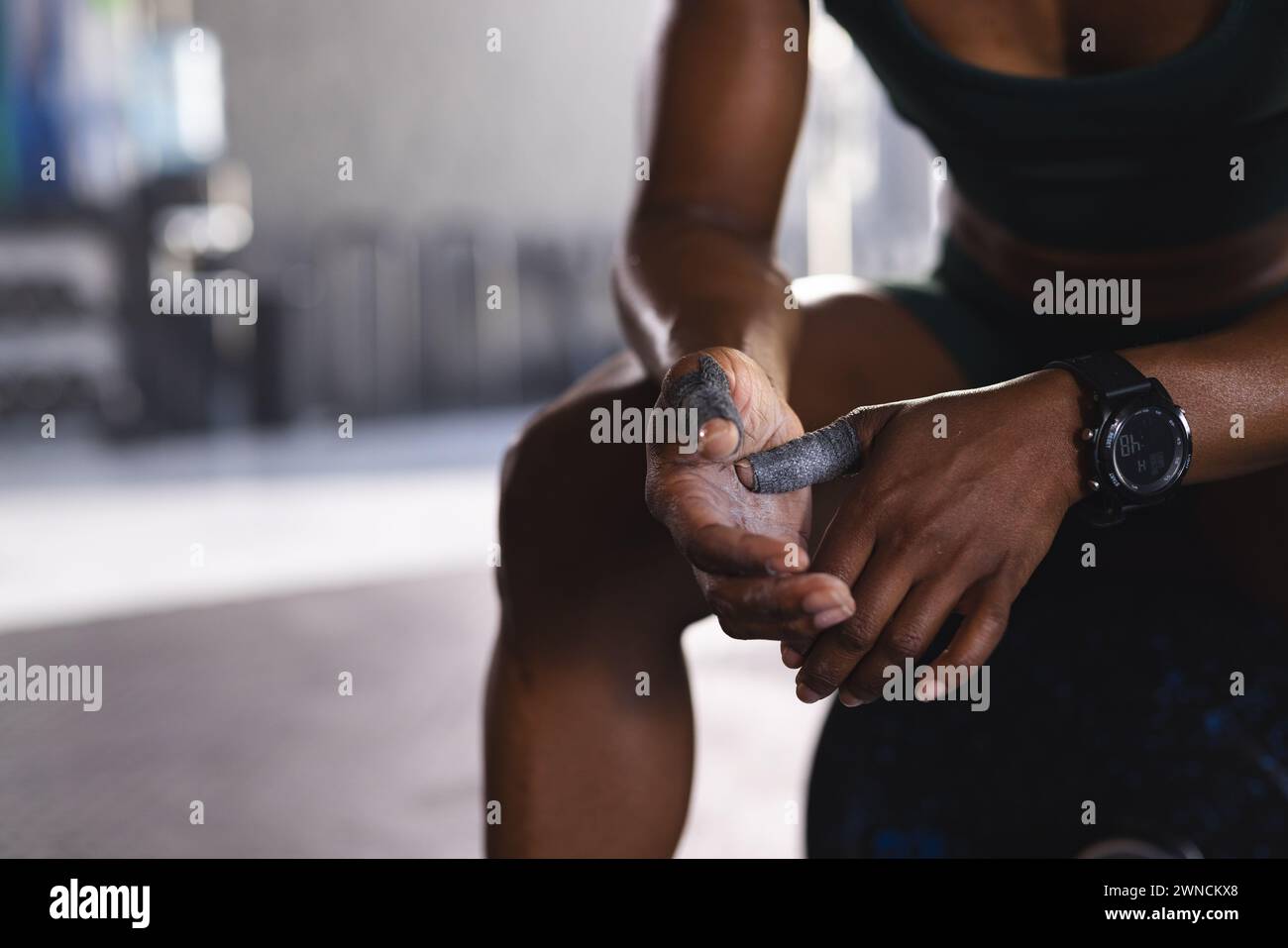 Gros plan d'une femme biraciale forte et en forme enveloppant sa main avec du ruban adhésif athlétique, avec espace de copie Banque D'Images