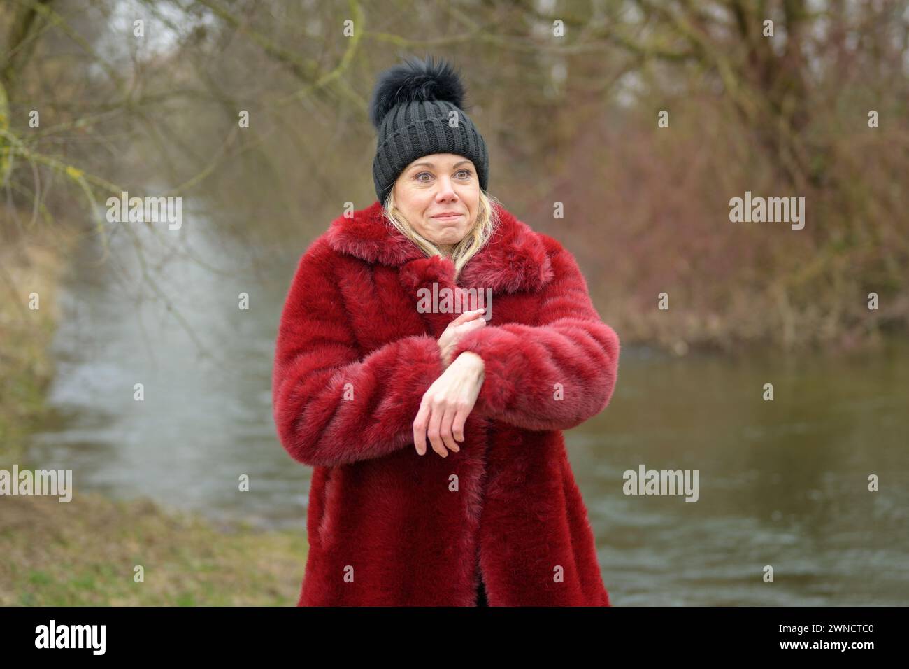 Jolie dame blonde portant une veste rouge et un chapeau noir bouffant faisant un visage drôle et pointant vers sa montre disant que quelqu'un est en retard Banque D'Images