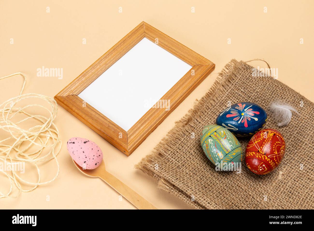 Oeufs de Pâques colorés sur un sac de sac et une cuillère en bois, un cadre photo et une corde sur le fond beige. Vue de dessus. Banque D'Images