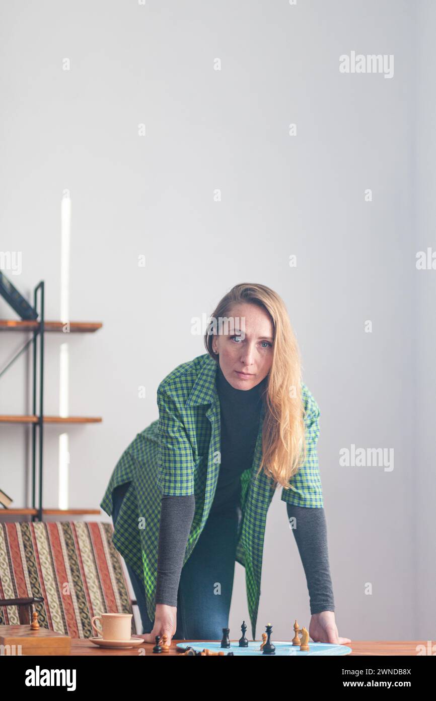 Composition verticale. Une femme déterminée se tient les mains sur la table et regarde attentivement devant elle. Sur la table, il y a des pièces d'échecs Banque D'Images