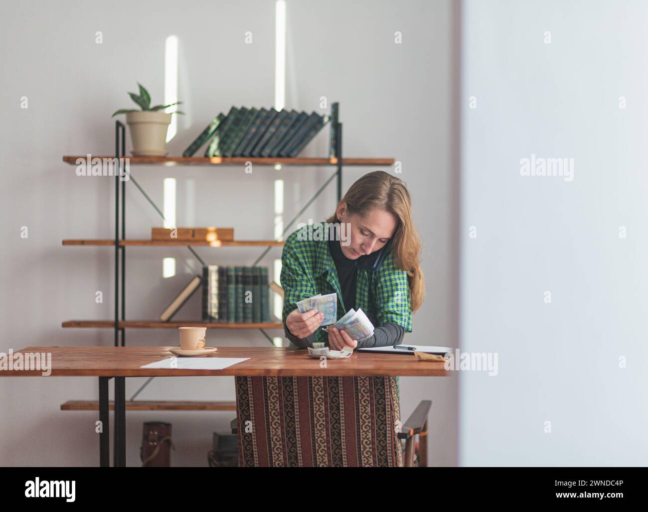 Une jeune jolie dame compte l'argent de façon réfléchie et attentive dans son bureau à domicile. Banque D'Images