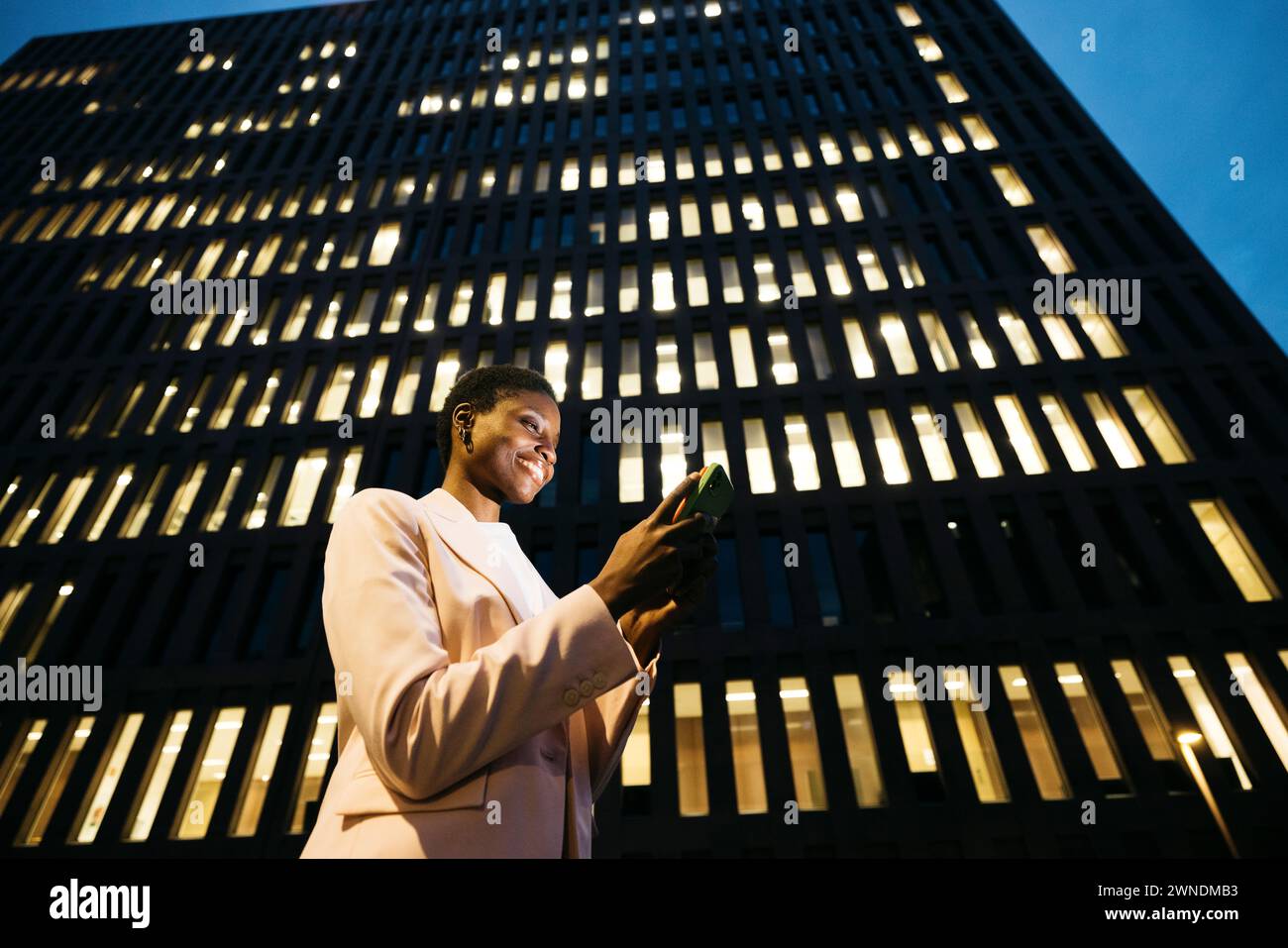 Jeune femme d'affaires élégante noire en face d'un bâtiment à l'aide d'un téléphone. Femme d'affaires avec un téléphone portable sur disctrict du centre-ville la nuit. Banque D'Images