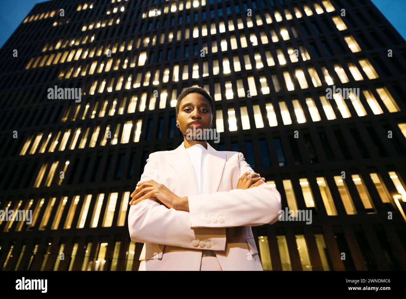 Jeune femme d'affaires élégante noire devant un bâtiment regardant la caméra. Femme d'affaires sur disctrict du centre-ville la nuit. Banque D'Images