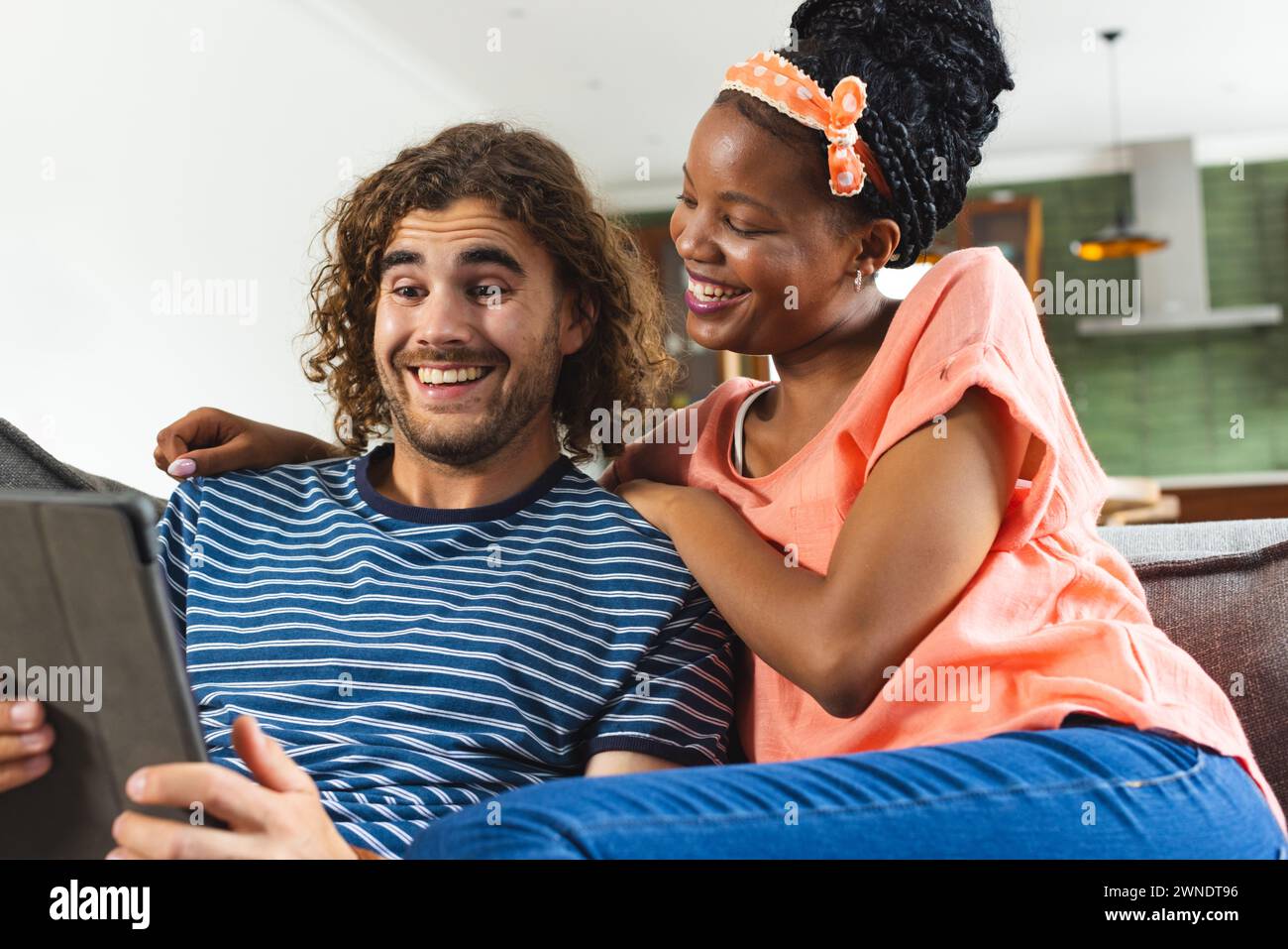 Couple diversifié jeune femme afro-américaine et jeune homme caucasien partagent une tablette, souriant ensemble Banque D'Images