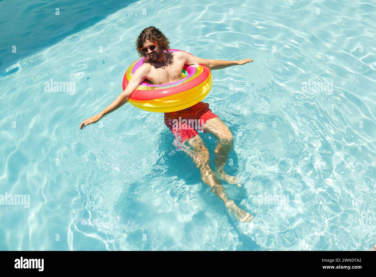 Jeune homme caucasien profite d'une journée ensoleillée dans la piscine avec un anneau de flotteur coloré Banque D'Images