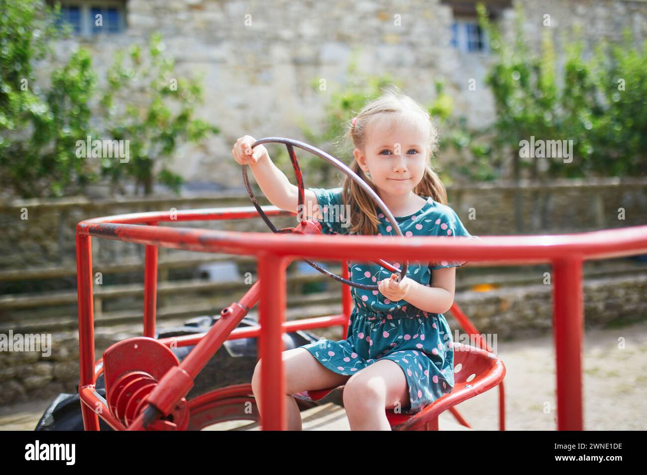 Adorable fille d'enfant d'âge préscolaire jouant sur le vieux tracteur rouge sur la ferme Gally près de Paris, France. Activités estivales en plein air pour les enfants Banque D'Images