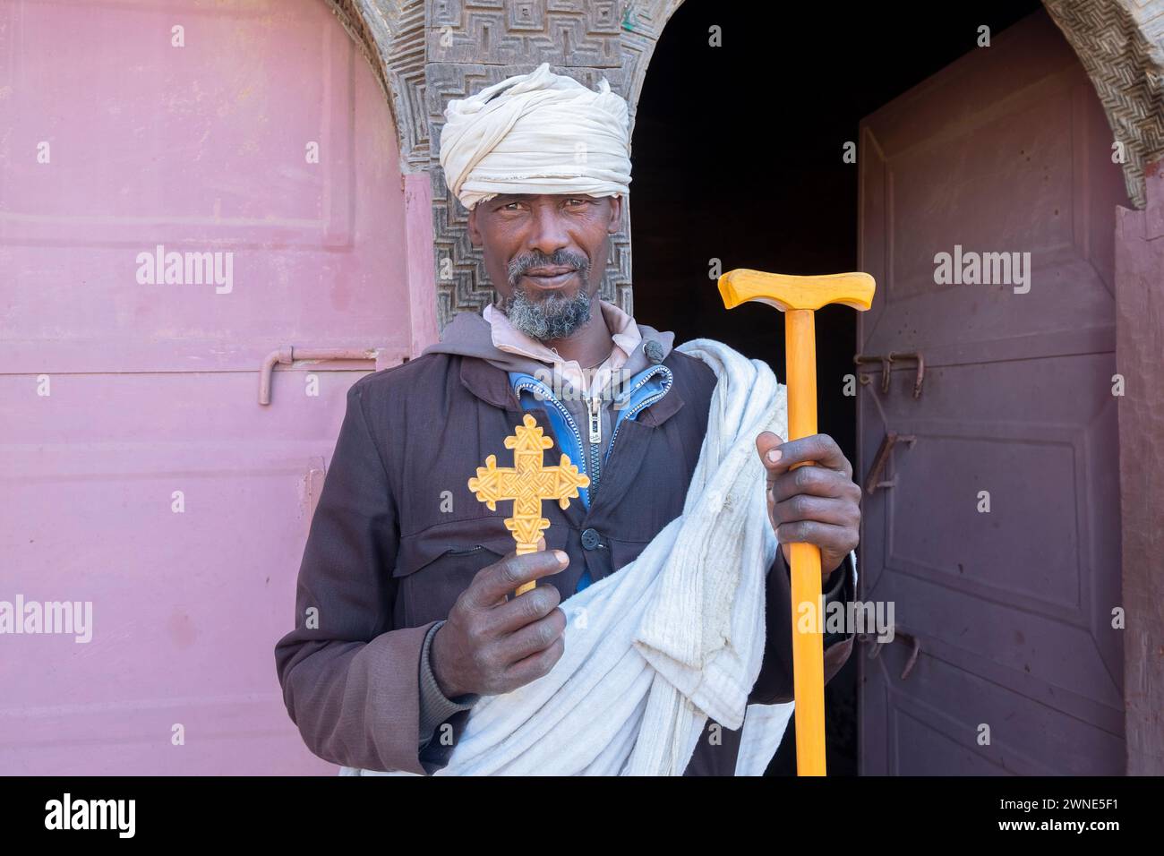 Homme éthiopien vieux prêtre en vêtements traditionnels tenant un bâton et une croix de main dans sa main devant une porte. Ethiopie Banque D'Images