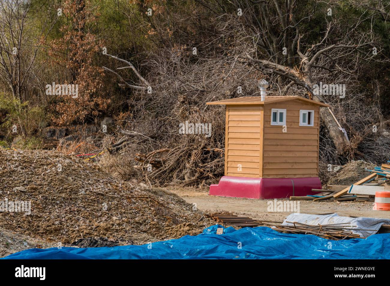 Toilettes publiques devant un arbre abattu entouré de barres d'armature et d'autres matériaux sur un chantier de construction rural en Corée du Sud Banque D'Images