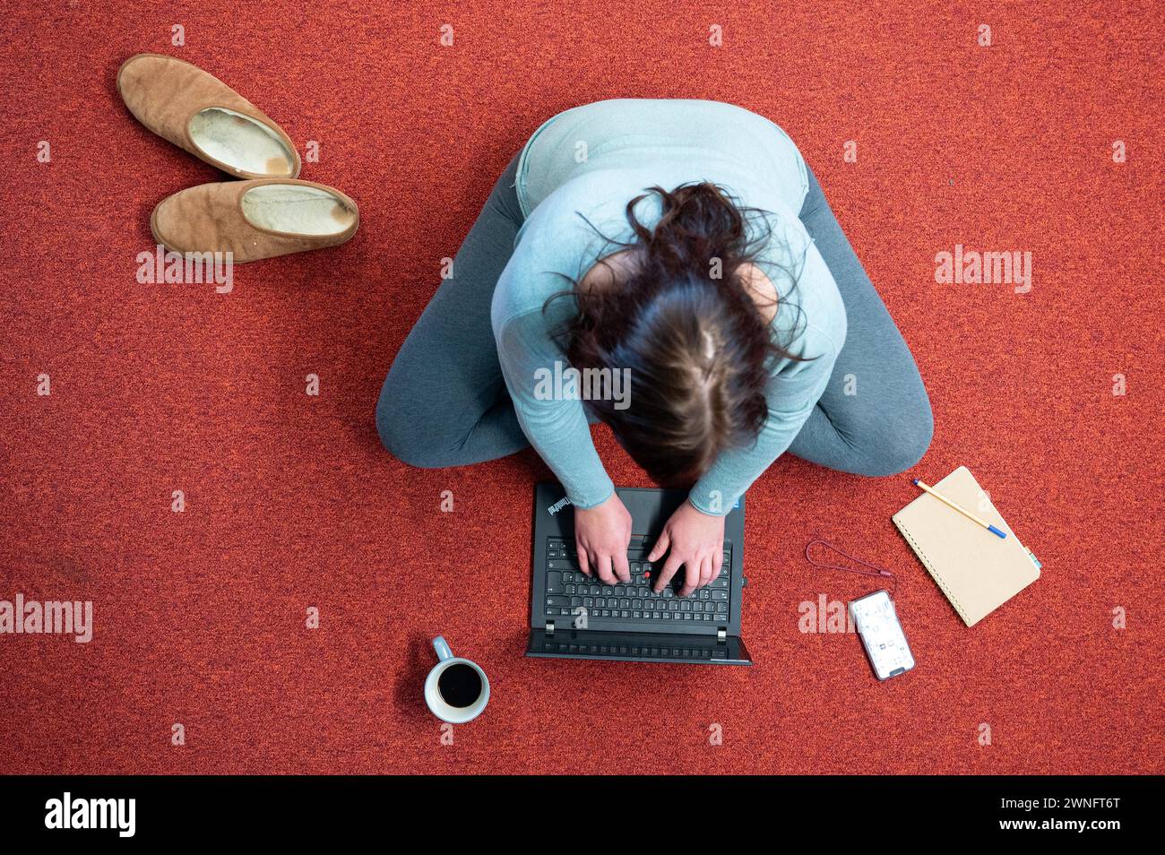Dresde, Allemagne. 02 mars 2024. Une femme est assise sur un tapis dans son bureau à domicile et travaille sur un ordinateur portable (scène mise en scène). Crédit : Sebastian Kahnert/dpa/Alamy Live News Banque D'Images