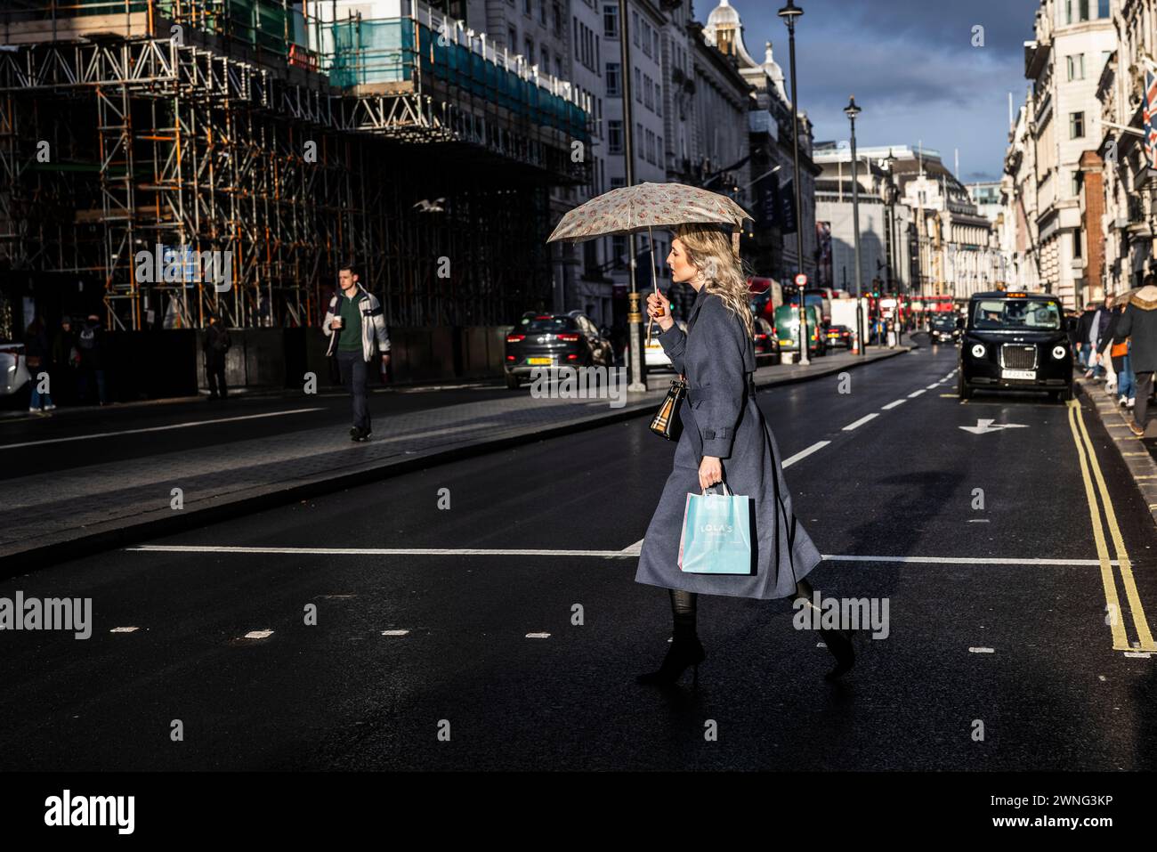 Une femme traverse Piccadilly à Mayfair tenant son parapluie pendant une averse de pluie, Londres, Angleterre, Royaume-Uni Banque D'Images