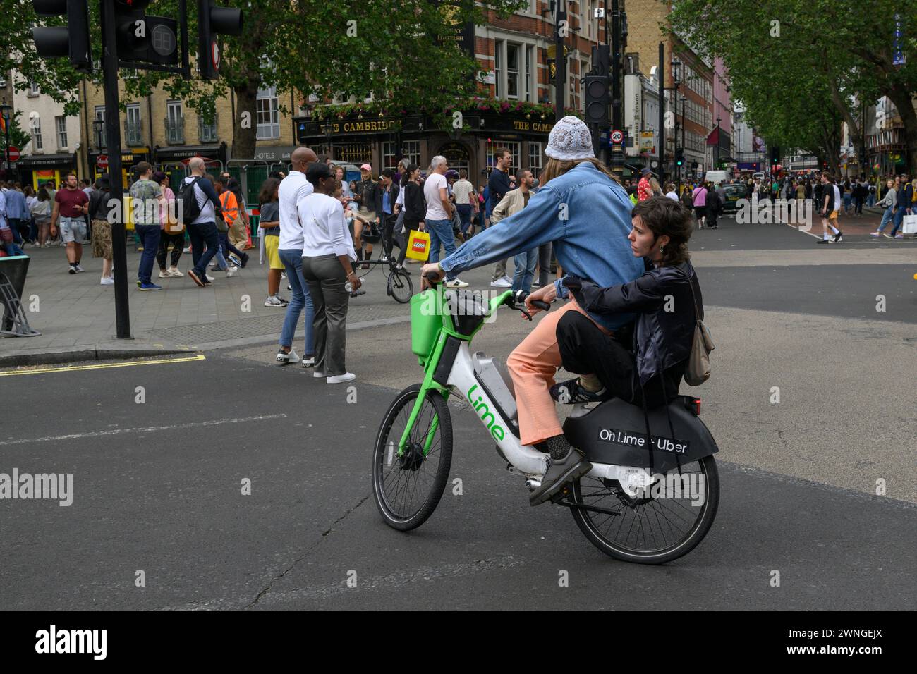 Un homme et une femme passager pilote sur un vélo de location électrique Lime à travers Cambridge Circus, Charing Cross Road, Londres, Royaume-Uni. 1er juillet 2023 Banque D'Images