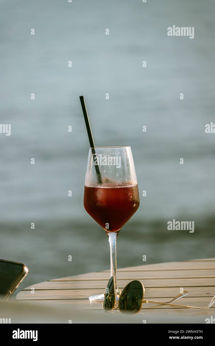 Escena elegante y relajada, una mesa sobre la que destaca una copa de vino. Al lado de la copa Hay un par de gafas de sol. Se aprecia un Móvil Banque D'Images