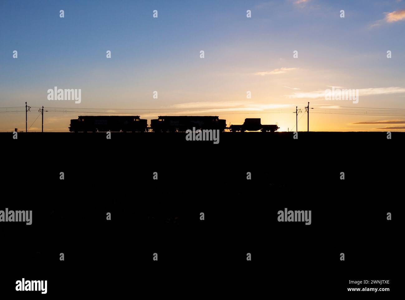 Une silhouette de 2 locomotives diesel de classe 37 de Direct Rail services English Electric tirant des flacons nucléaires sur la ligne principale de la côte ouest au coucher du soleil Banque D'Images