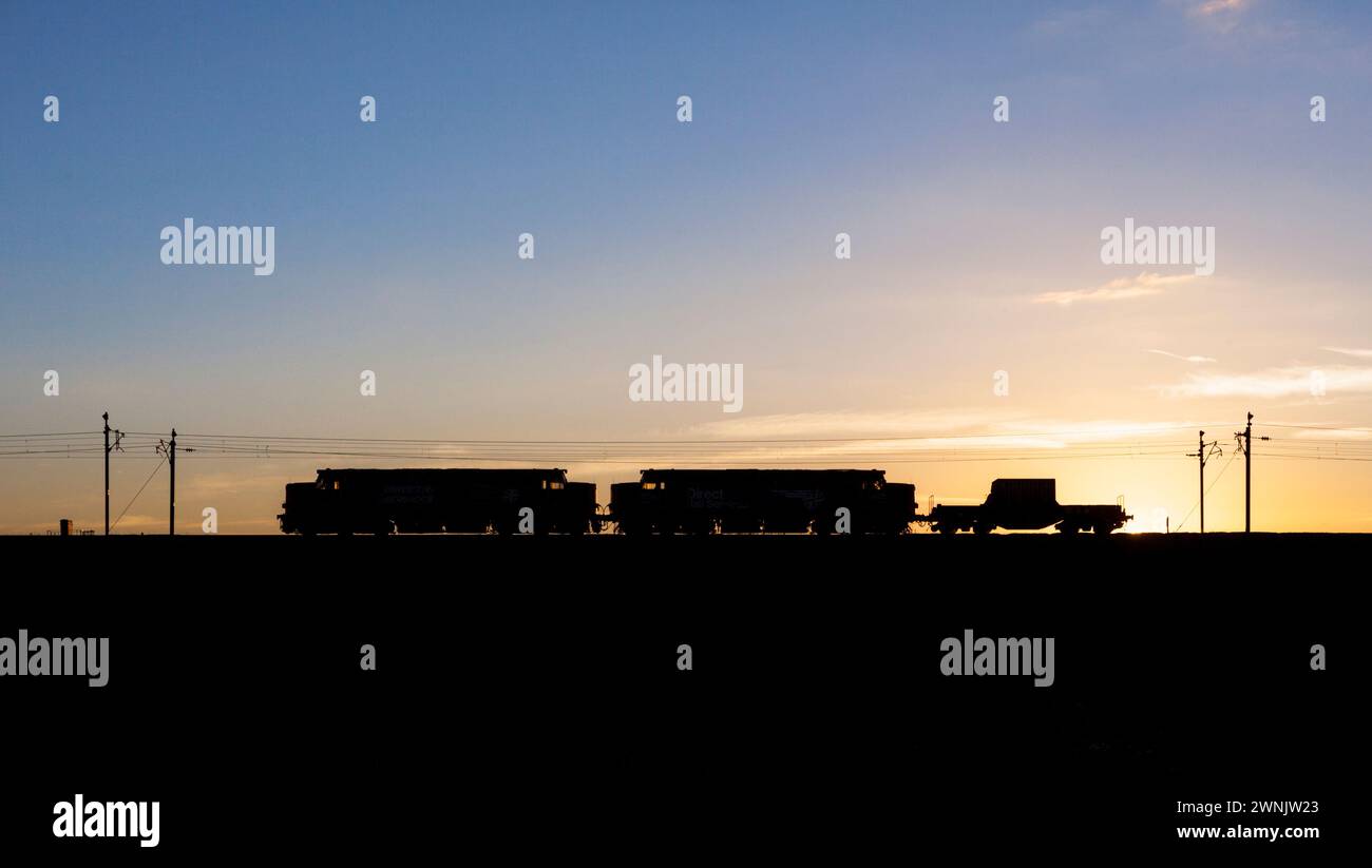 Une silhouette de 2 locomotives diesel de classe 37 de Direct Rail services English Electric tirant des flacons nucléaires sur la ligne principale de la côte ouest au coucher du soleil Banque D'Images