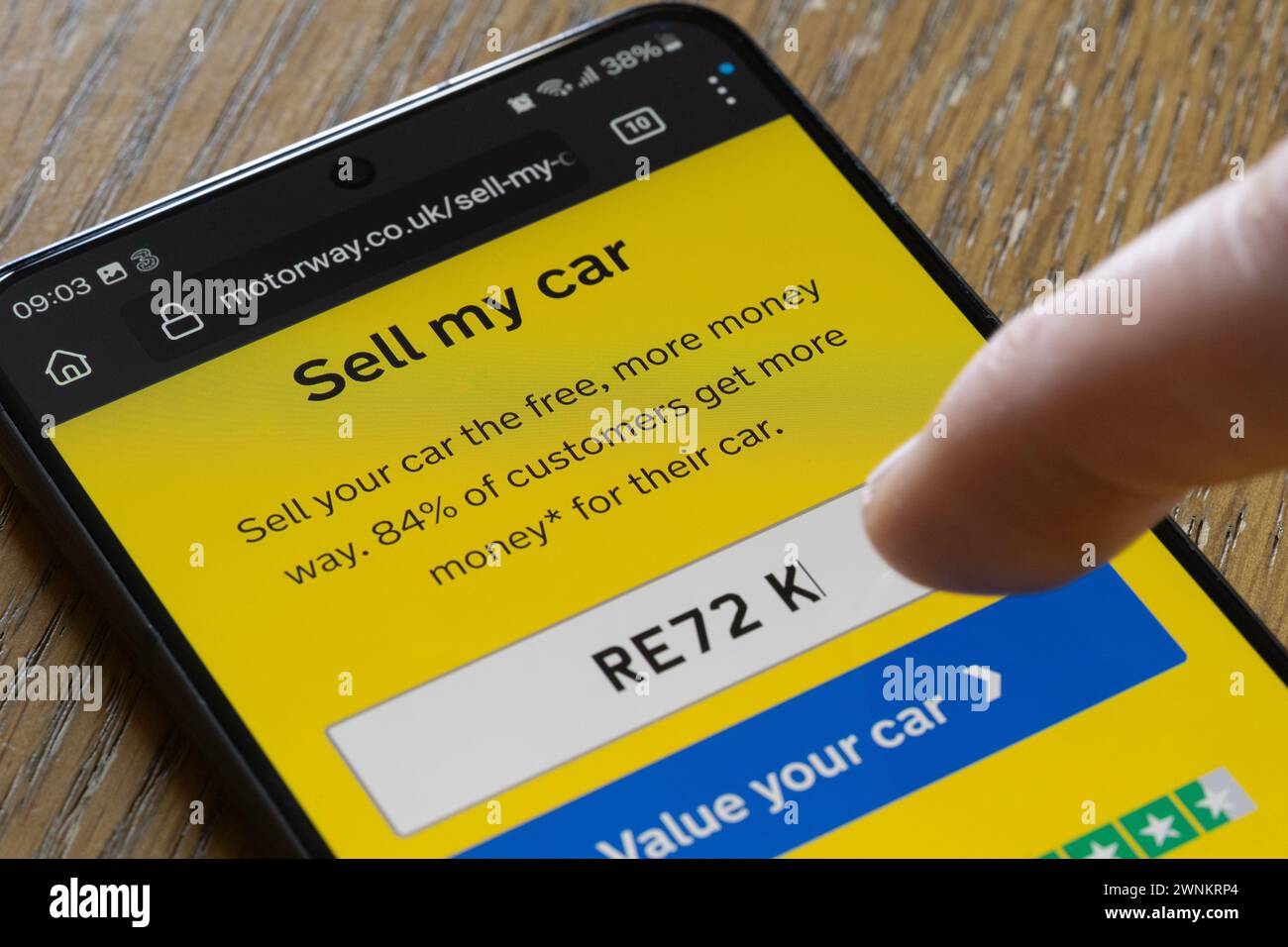 Un homme saisissant son numéro d'immatriculation de voiture dans l'application de vente de voitures d'autoroute sur son smartphone, Royaume-Uni. L'écran affiche « vendre ma voiture » et comporte un bouton de devis Banque D'Images