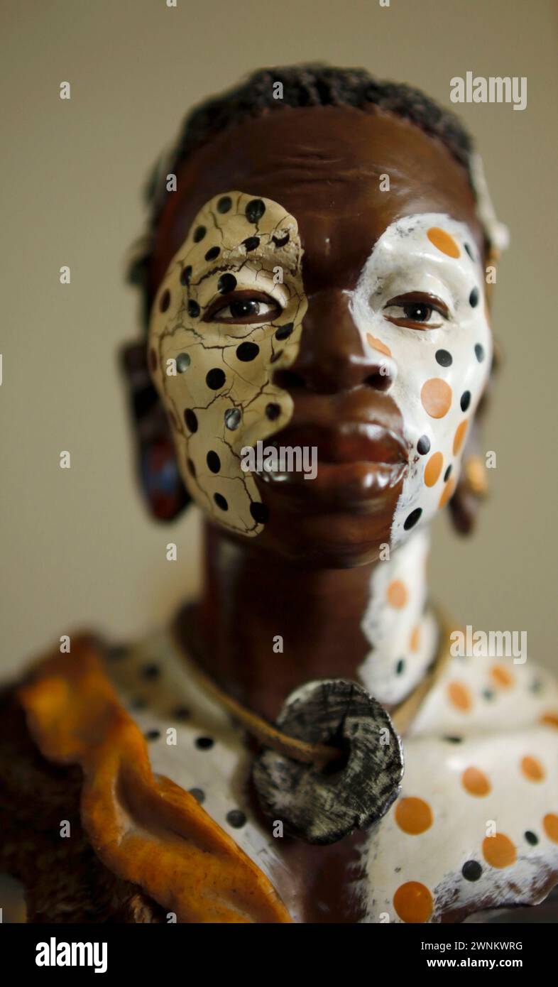 Gros plan d'une figurine africaine colorée à motifs avec un maquillage tribal complexe, sur un fond flou. Banque D'Images