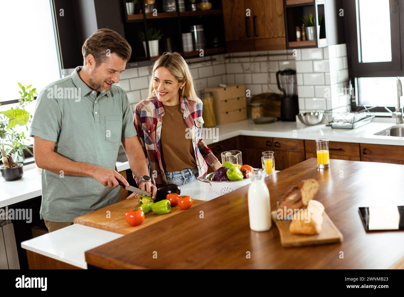 Un homme et une femme souriants hachant des légumes frais sur un îlot de cuisine, profitant d'une activité culinaire saine ensemble Banque D'Images