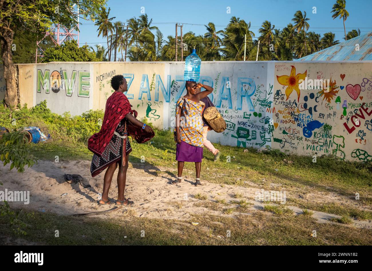 Une femme porte un récipient d'eau sur la tête et discute avec un guerrier Massaï à Jambiani, Zanzibar, Tanzanie Banque D'Images Une femme porte un récipient d'eau sur la tête et discute avec un guerrier Massaï à Jambiani, Zanzibar, Tanzanie Banque D'Images