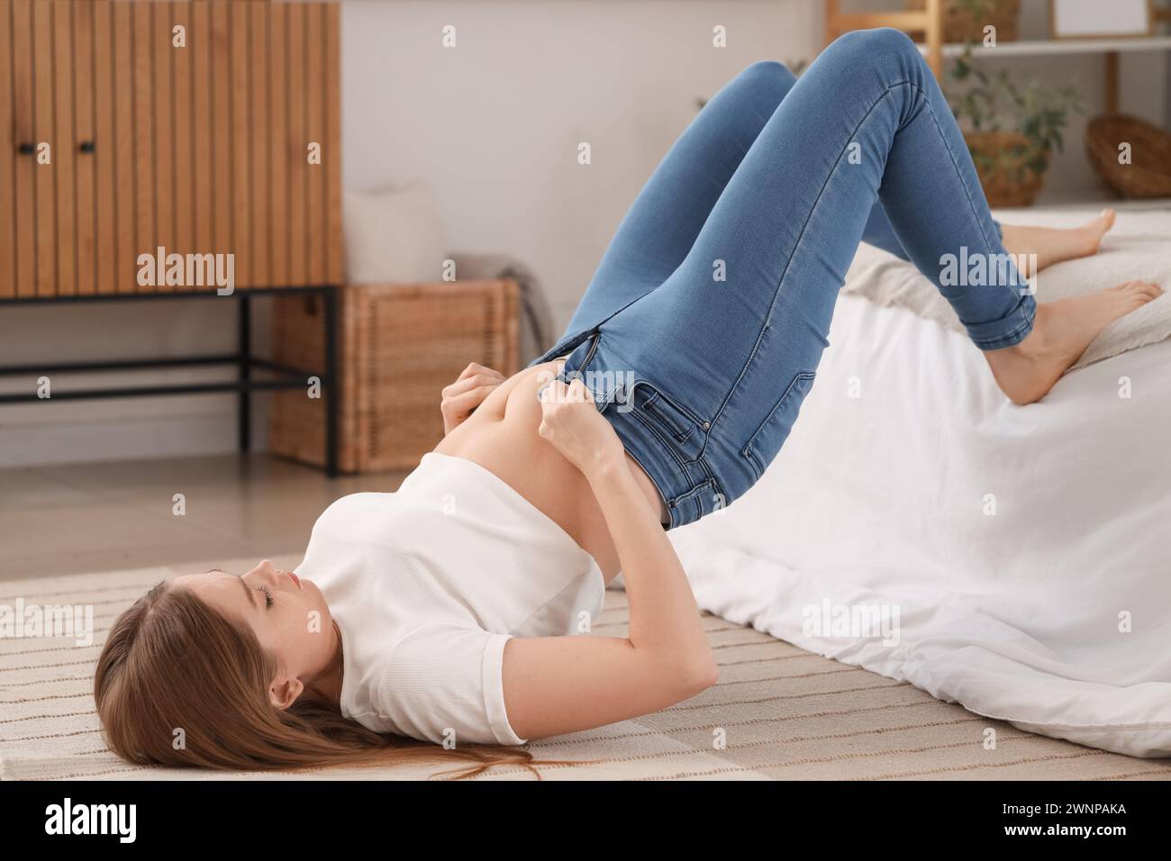 Jeune femme essayant de boutonner des jeans serrés dans la chambre. Concept de gain de poids Banque D'Images