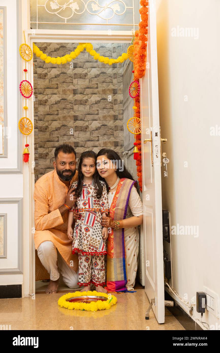 Heureuse famille indienne de trois faisant grah pravesh rituel ou entrant dans une nouvelle maison pour la première fois. Famille assise devant un kumk liquide rempli d'assiette Banque D'Images