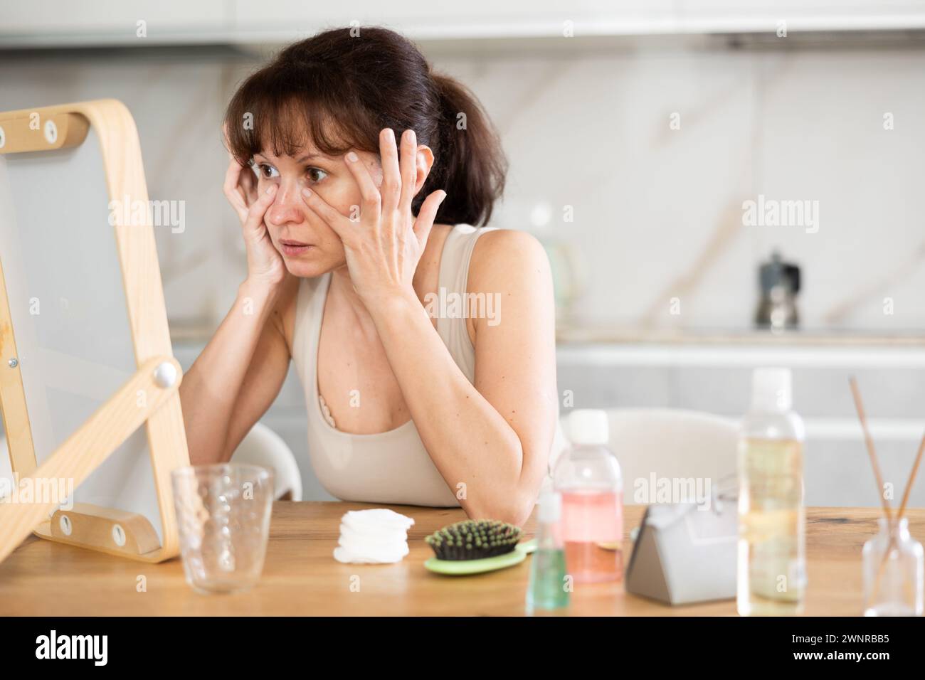 Femme inspectant la peau du visage dans le miroir pendant la routine quotidienne Banque D'Images