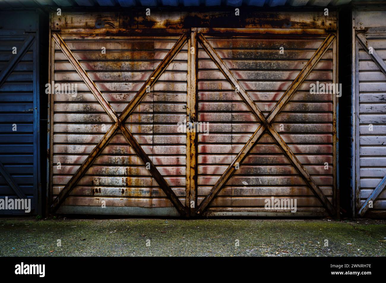 Vieille porte de garage métallique en tôle ondulée verrouillée avec cadenas, surface usée et rouillée Banque D'Images