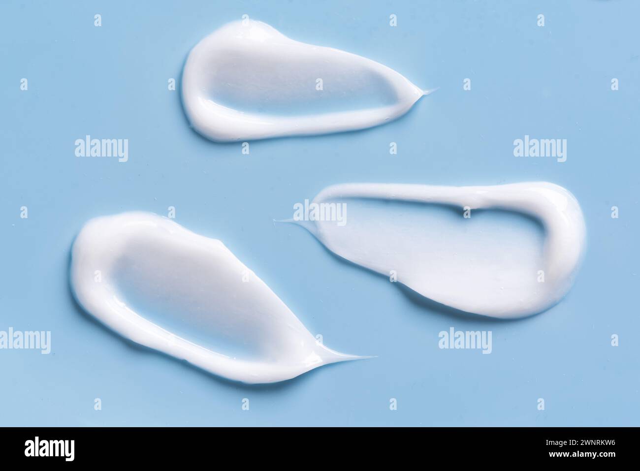 Motif de maculage de taches de crème cosmétique blanche sur fond bleu. Ensemble de coups de produit cosmétique en gel léger. Banque D'Images