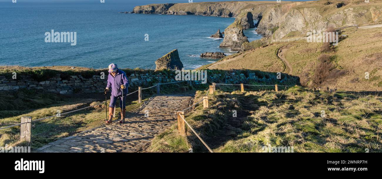 Une image panoramique d'une femme mature utilisant des bâtons de marche pour l'aider à marcher jusqu'à un sentier de Bedruthan Steps sur la spectaculaire côte nord de Cornwall Banque D'Images