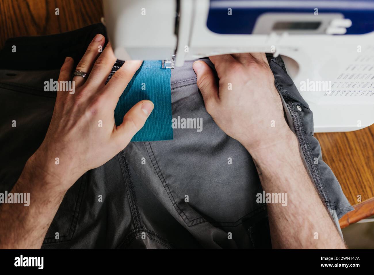 Au-dessus du plan de l'homme assis à la table de la cuisine réparant pantalon de travail Banque D'Images