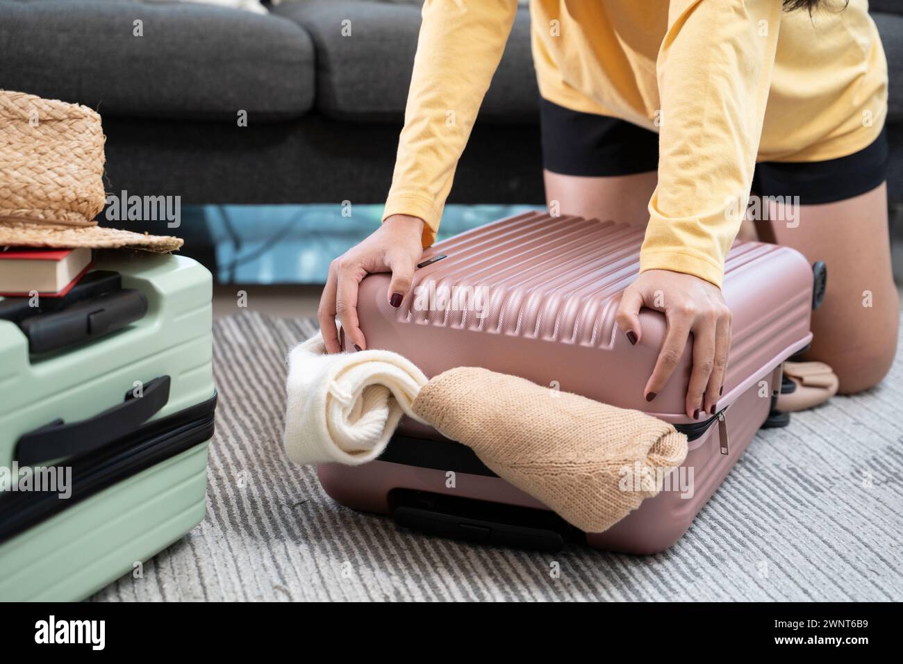 Jeune femme asiatique empilant des vêtements et dans un étui de sac, essayant d'emballer un bagage à main. Banque D'Images