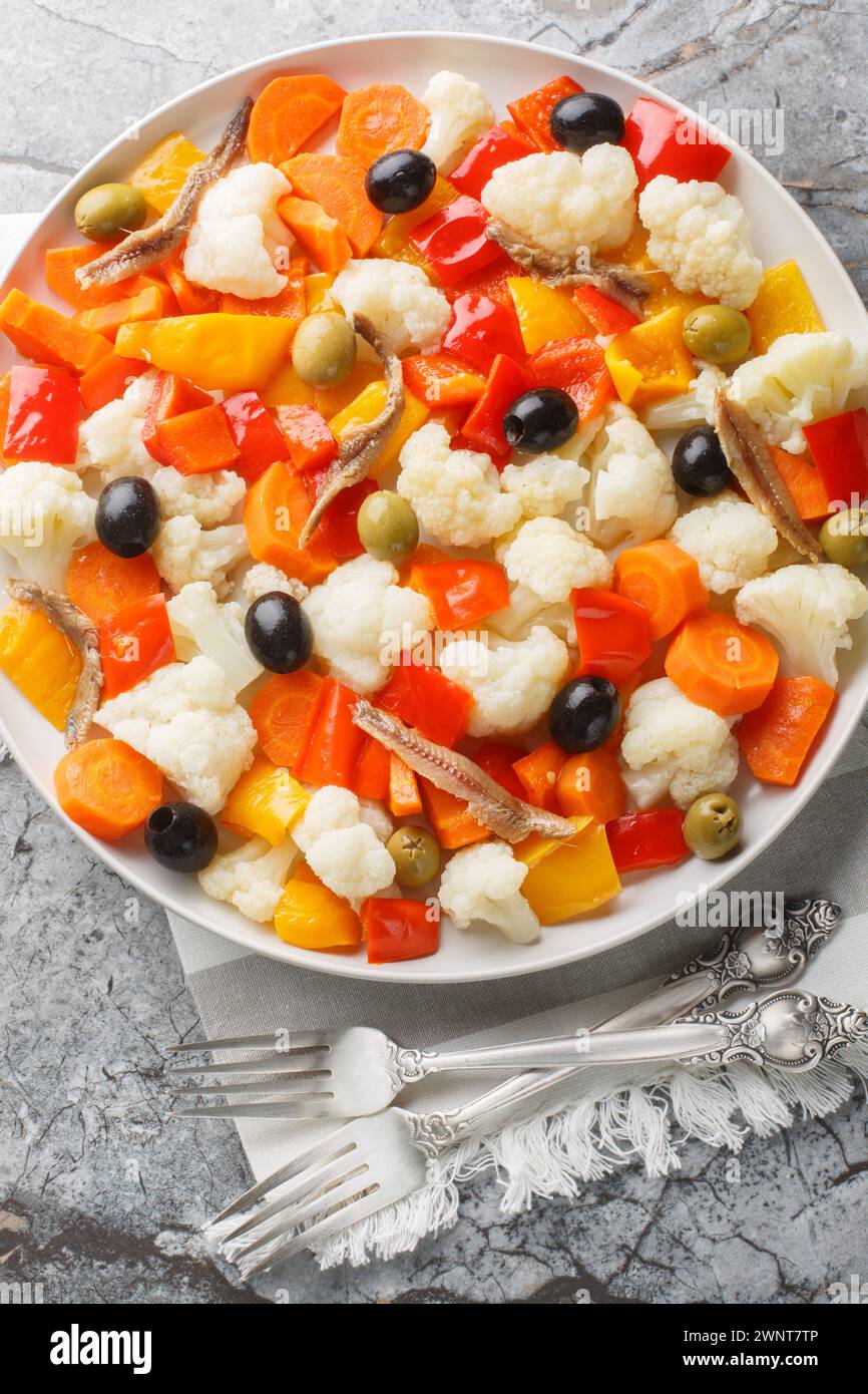 Insalata Di Rinforzo salade italienne de chou-fleur avec giardiniera, olives et anchois gros plan sur l'assiette sur la table. Vue de dessus verticale Banque D'Images